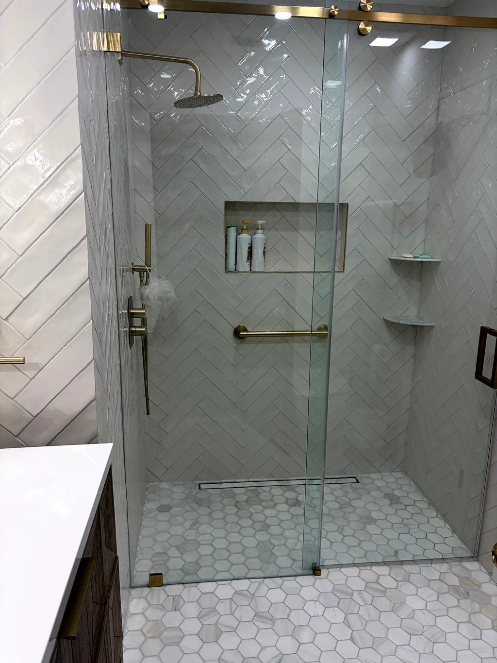 Walk-in shower in large-format marble-look porcelain with brushed brass fixtures, frameless glass and a hexagonal mosaic floor