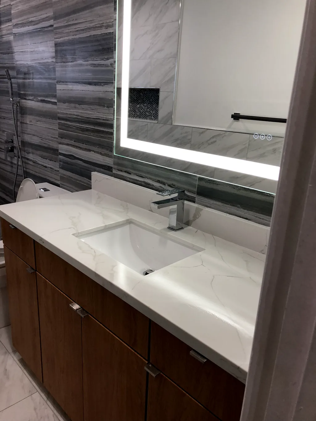 Floating vanity with a backlit LED mirror against a wood-look porcelain feature wall