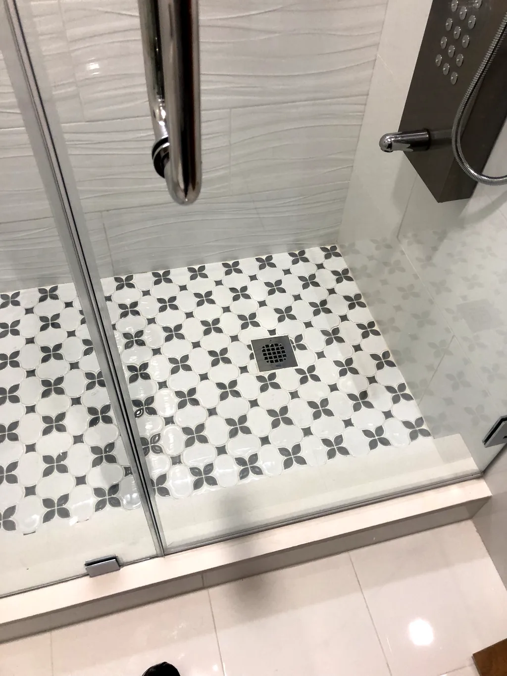 Patterned encaustic-look mosaic shower floor behind frameless glass