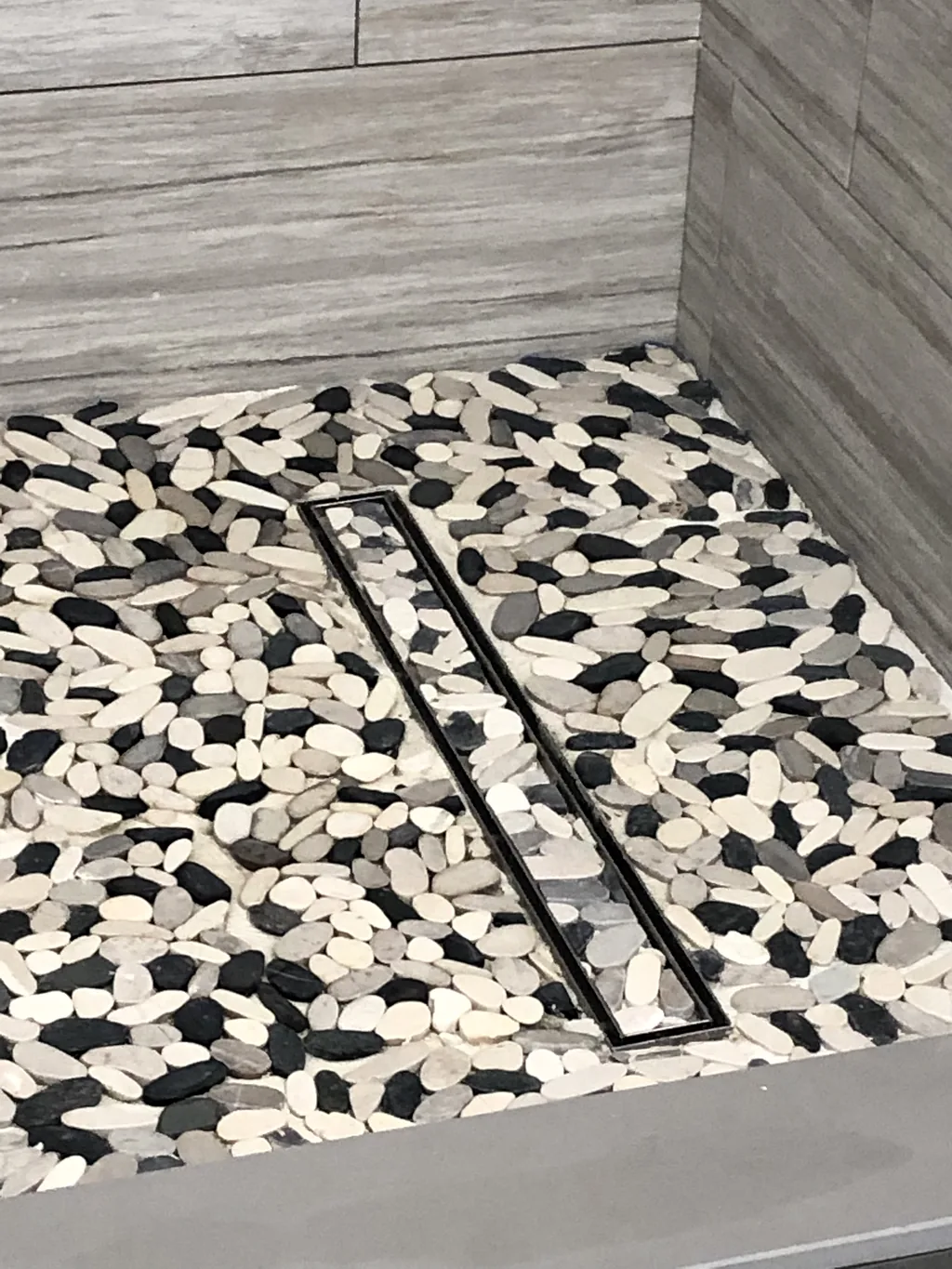 Black and white pebble mosaic shower floor set around a linear drain