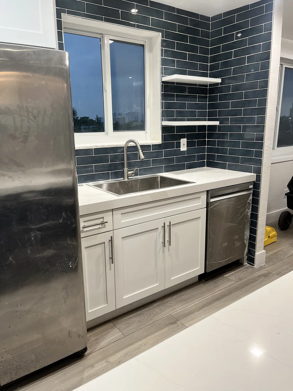 Kitchen run with a blue glass subway tile backsplash, stainless appliances and white quartz counters