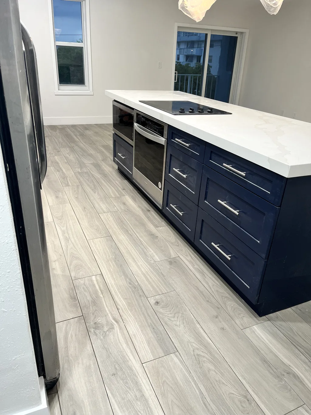 Navy shaker kitchen island with a white quartz waterfall top over wood-look plank flooring