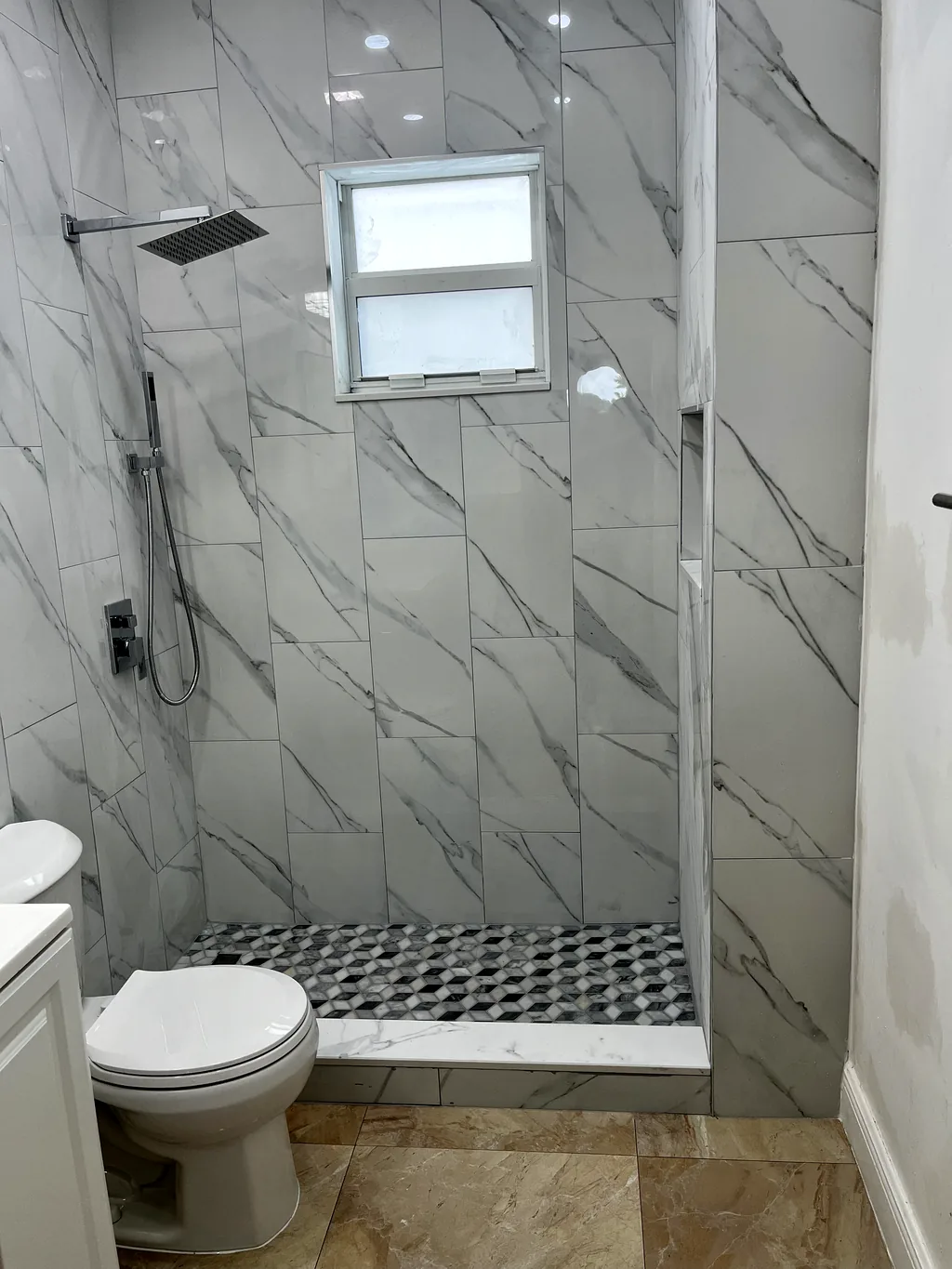 Marble-look shower surround with a mosaic floor and a recessed shelf